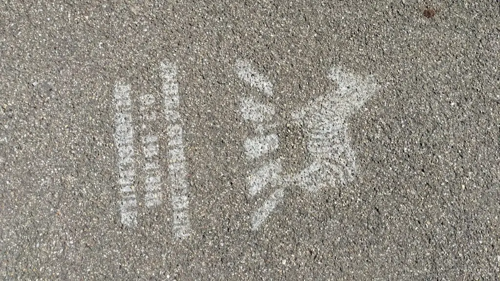 Weiße Kreidezeichnungen auf dem Pflaster zeigen eine vertikale Linie aus Kreisen und Rechtecken auf der linken Seite und ein stilisiertes geflügeltes Tier, möglicherweise ein Pferd oder einen Pegasus, auf der rechten Seite. Die Oberfläche ist rauer grauer Asphalt.