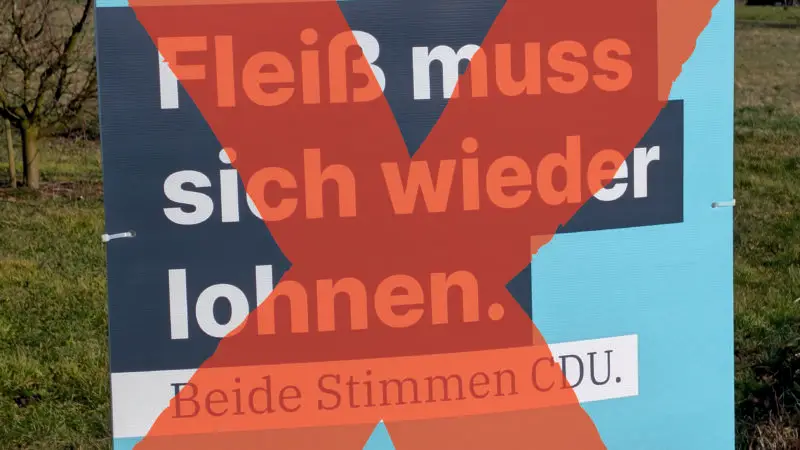 Ein CDU-Wahlplakat mit dem Slogan Fleiß muss sich wieder lohnen. Beide Stimmen CDU. wird durch ein großes rotes X verunstaltet, das darüber gemalt wird. Das Plakat ist an einem Mast im Freien angebracht.