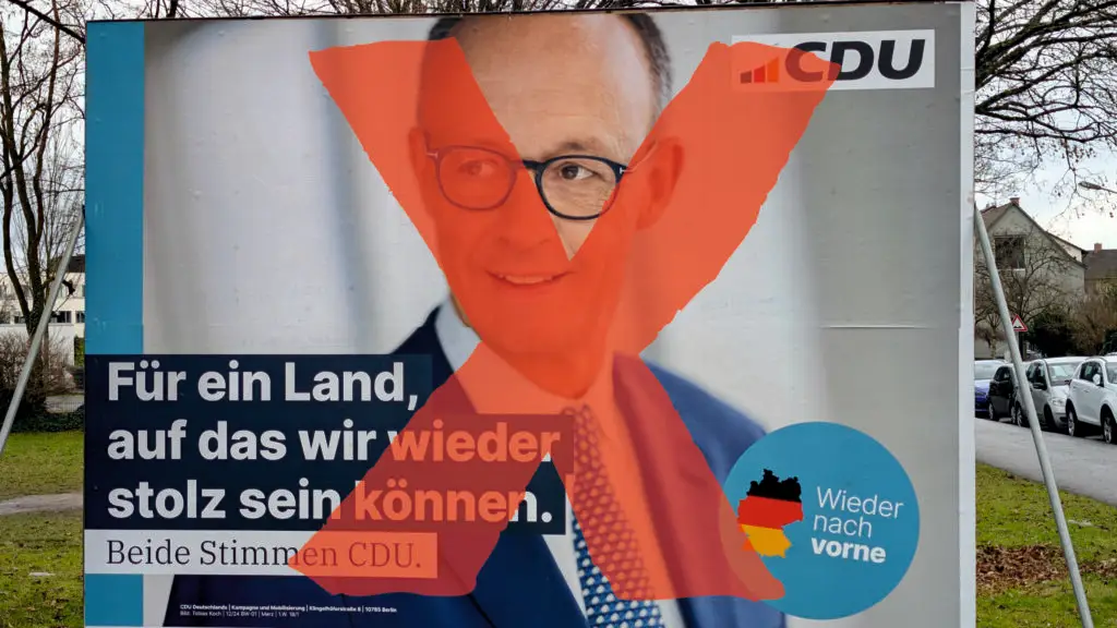 Ein CDU-Wahlkampfplakat, auf dem ein Mann mit Anzug und Brille zu sehen ist, wird mit einem großen roten X verunstaltet, das über sein Gesicht gemalt wird. Der Text lautet: Für ein Land, auf das wir wieder stolz sein können. Beide Stimmen CDU.