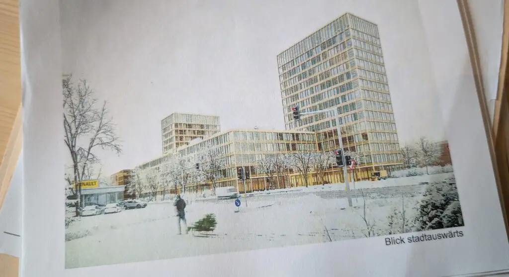 Eine Person steht auf einem verschneiten Gehweg in der Nähe einer Straße mit Autos, Bäumen und modernen Hochhäusern im Hintergrund. Die Szene ist städtisch, und der Himmel ist bedeckt. Der Text Blick stadtauswärts erscheint unten rechts.