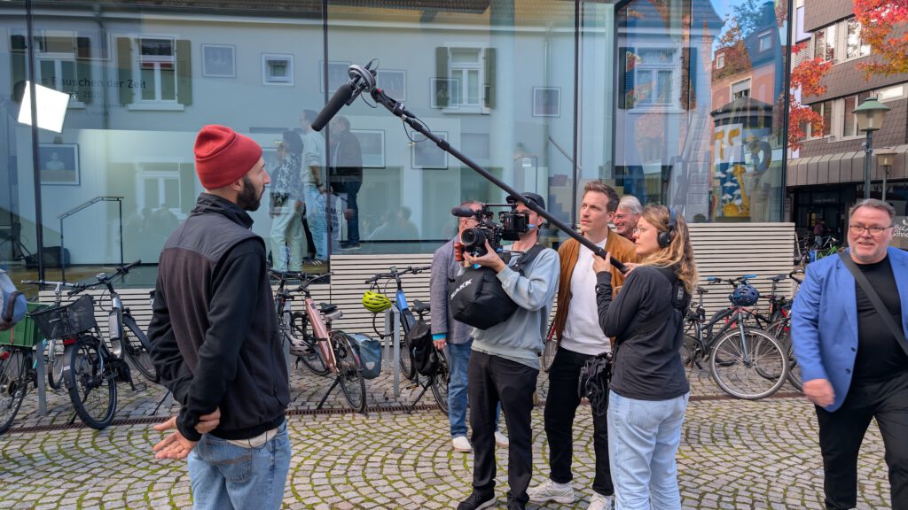 Elias Errerd mit roter Mütze wird von einem Filmteam mit Kameras und Mikrofonen vor dem Salmen interviewt.