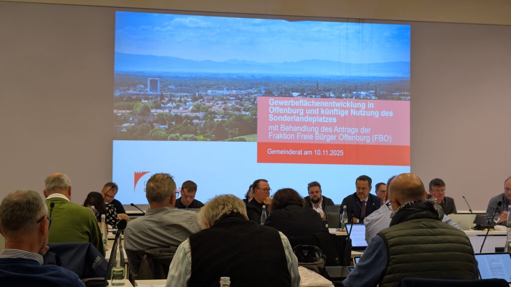 Der Gemeinderat sitzt an Tischen im Salmen und blickt auf einen großen Bildschirm, auf dem eine Präsentation über Gewerbeflächenentwicklung in Offenburg vom 11. November 2025 gezeigt wird.