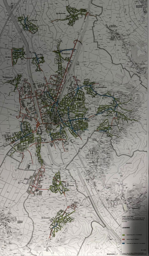 Die Karte zeigt eine Stadt mit Straßen, Autobahnen, Grünflächen und Wasserwegen. Die Legende unten rechts zeigt verschiedene Zonen an. In der Mitte befinden sich dicht besiedelte Gebiete, an den Rändern gibt es mehr verstreute Gebiete.