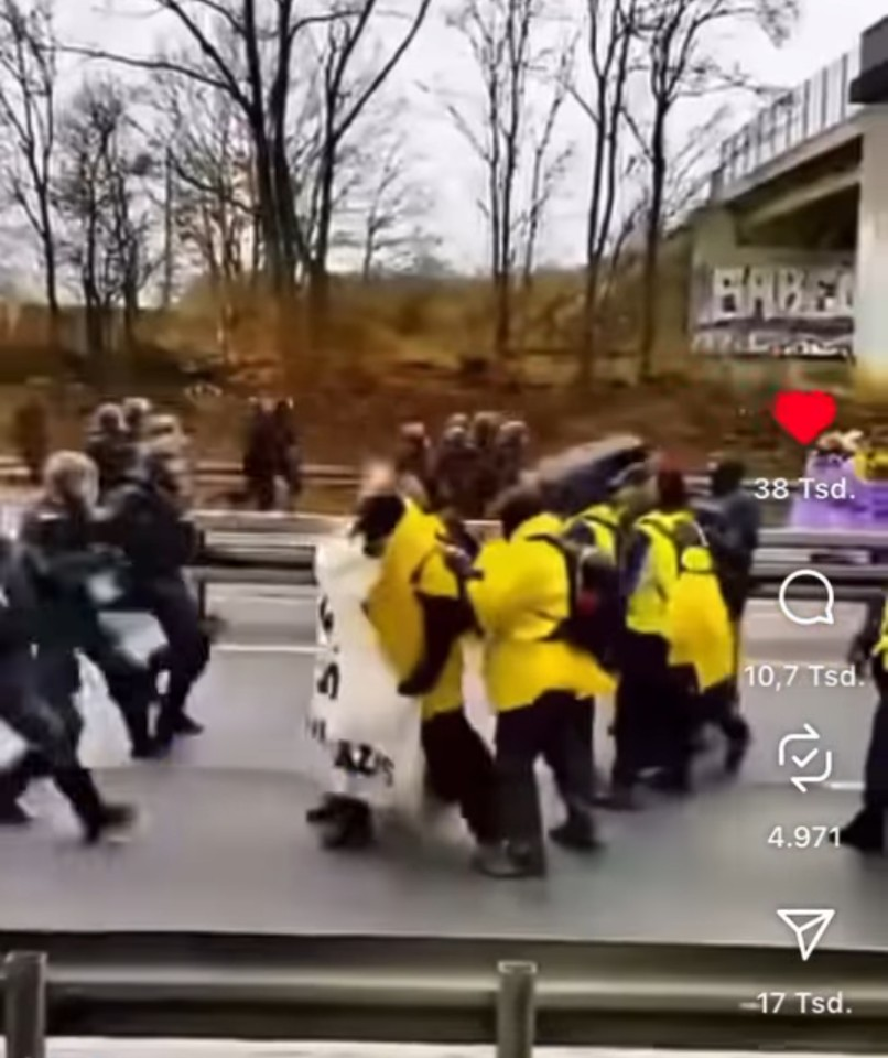 Eine Gruppe von Personen in gelben Jacken und dunkler Kleidung wird von Polizeibeamten angegriffen. Einige halten ein Transparent. Im Hintergrund sind Bäume und eine Überführung zu sehen. Auf der rechten Seite sind Symbole für soziale Medien zu sehen.
