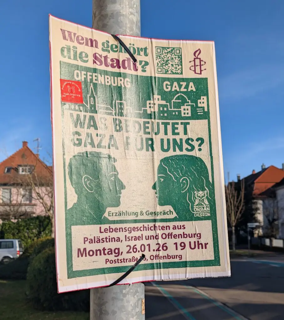 Ein Plakat an einem Straßenmast wirbt für eine Veranstaltung in Offenburg mit dem Titel Was bedeutet Gaza für uns? mit grünem und rotem Text, Illustrationen von zwei sprechenden Menschen, Datum, Uhrzeit und Amnesty International-Logo sichtbar. Häuser und blauer Himmel im Hintergrund.
