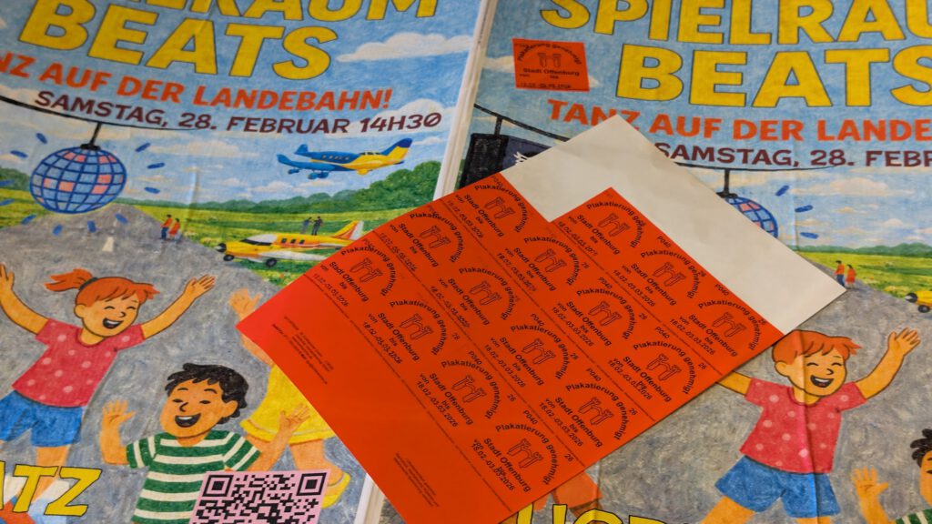 Ein Bogen orangefarbener Aufkleber mit schwarzer Schrift liegt auf bunten Plakaten, die für Spielraum Beats werben, eine Tanzveranstaltung am Samstag, den 28. Februar um 14:30 Uhr. Die Plakate zeigen tanzende Zeichentrickkinder und eine Discokugel.