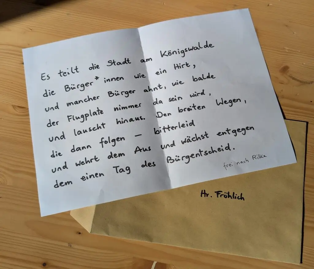 Ein geöffneter handgeschriebener Brief mit einem deutschen Gedicht liegt auf einem Holztisch. Daneben liegt ein versiegelter brauner Umschlag, adressiert an Hr. Fröhlich. Das Gedicht ist fein säuberlich mit schwarzer Tinte auf weißem Papier geschrieben.