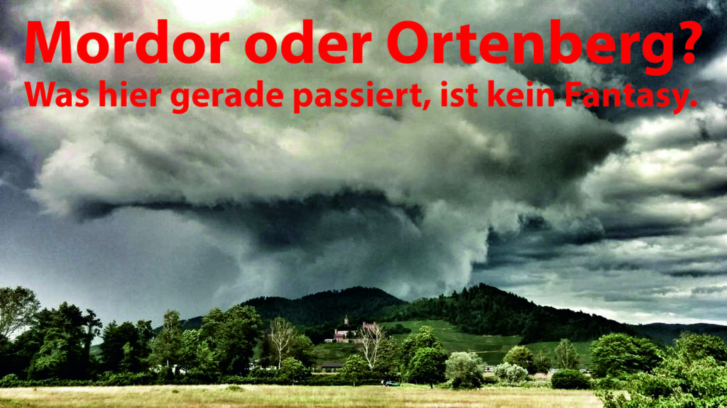 Eine dramatische, dunkle Gewitterwolke schwebt über einer grünen Landschaft um Schloss Ortenberg. Der fettgedruckte rote deutsche Text lautet: Mordor oder Ortenberg? Was hier gerade passiert, ist keine Fantasie.