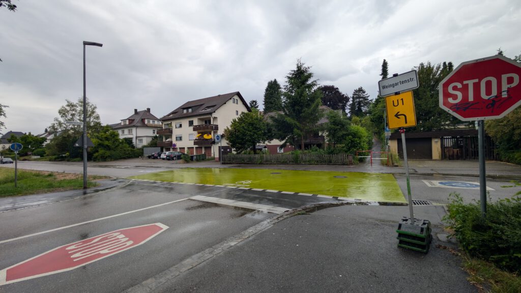 Intersection with a red STOP sign, yellow U-turn sign, damp pavement, and a green bike lane; residential buildings behind under an overcast sky.