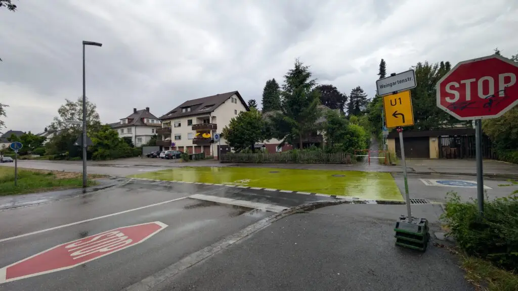 Intersection with a red STOP sign, yellow U-turn sign, damp pavement, and a green bike lane; residential buildings behind under an overcast sky.