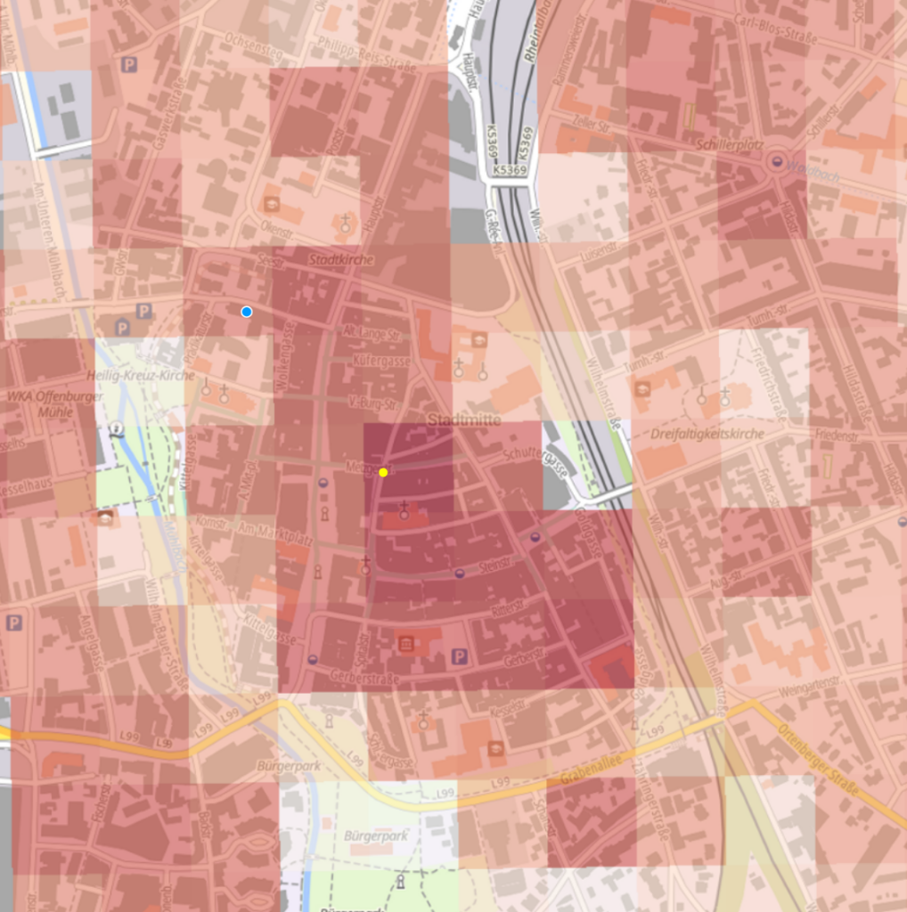 Eine digitale Karte eines Stadtgebiets, die in verschiedenen Rottönen dargestellt ist und auf der Straßen, Parks und Sehenswürdigkeiten zu erkennen sind. Im Zentrum befindet sich ein dunkelrotes Quadrat mit einer gelben Markierung. Außerdem sind blaue Standortmarkierungen und ein blauer Punkt zu sehen.