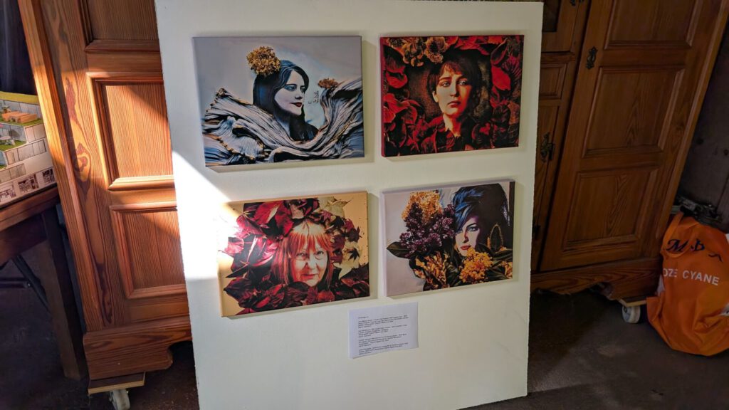 Eine Ausstellungswand mit vier gerahmten Porträts von Frauen, die mit Blumen geschmückt sind, vor dem Hintergrund eines Holzschranks und einer orangefarbenen Tasche in einem warm beleuchteten Raum. Unter den Porträts befindet sich eine kurze Beschreibung.
