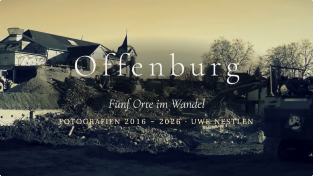Ein sepiafarbenes Bild zeigt eine Baustelle in Offenburg mit schweren Maschinen und Gebäuden im Hintergrund. Der eingeblendete Text lautet: Offenburg, Fünf Orte im Wandel, Fotografien 2016–2026, Uwe Nestlen.